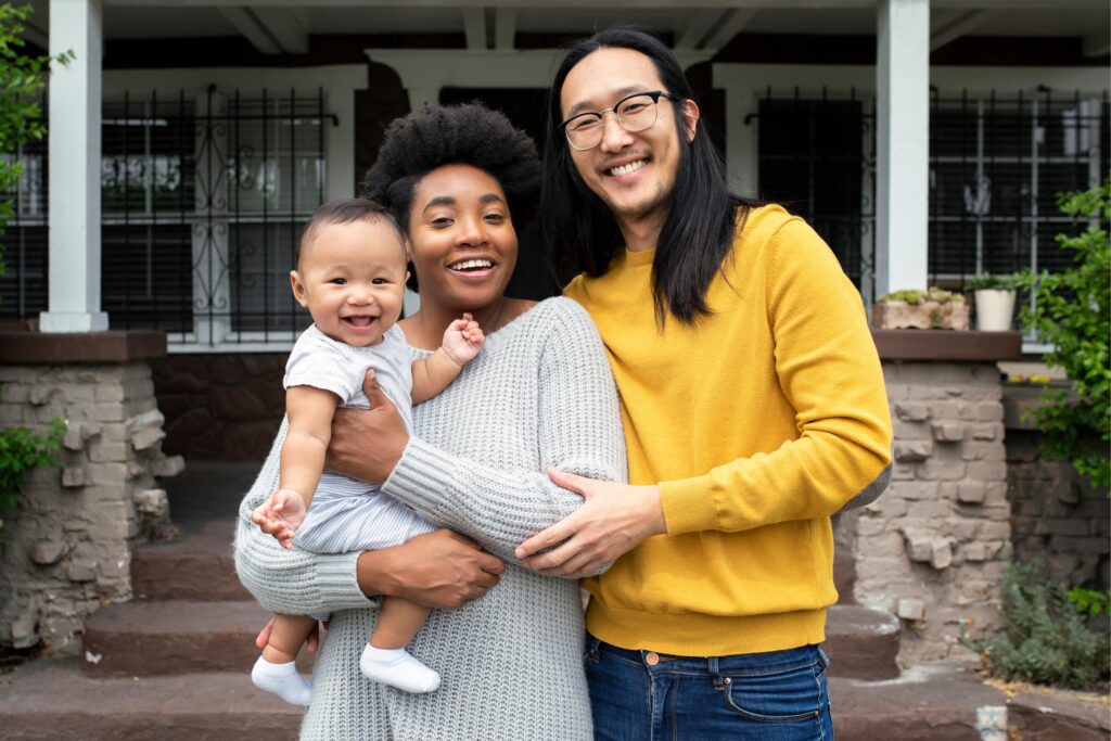 Happy couple with their infant standing in front of their home