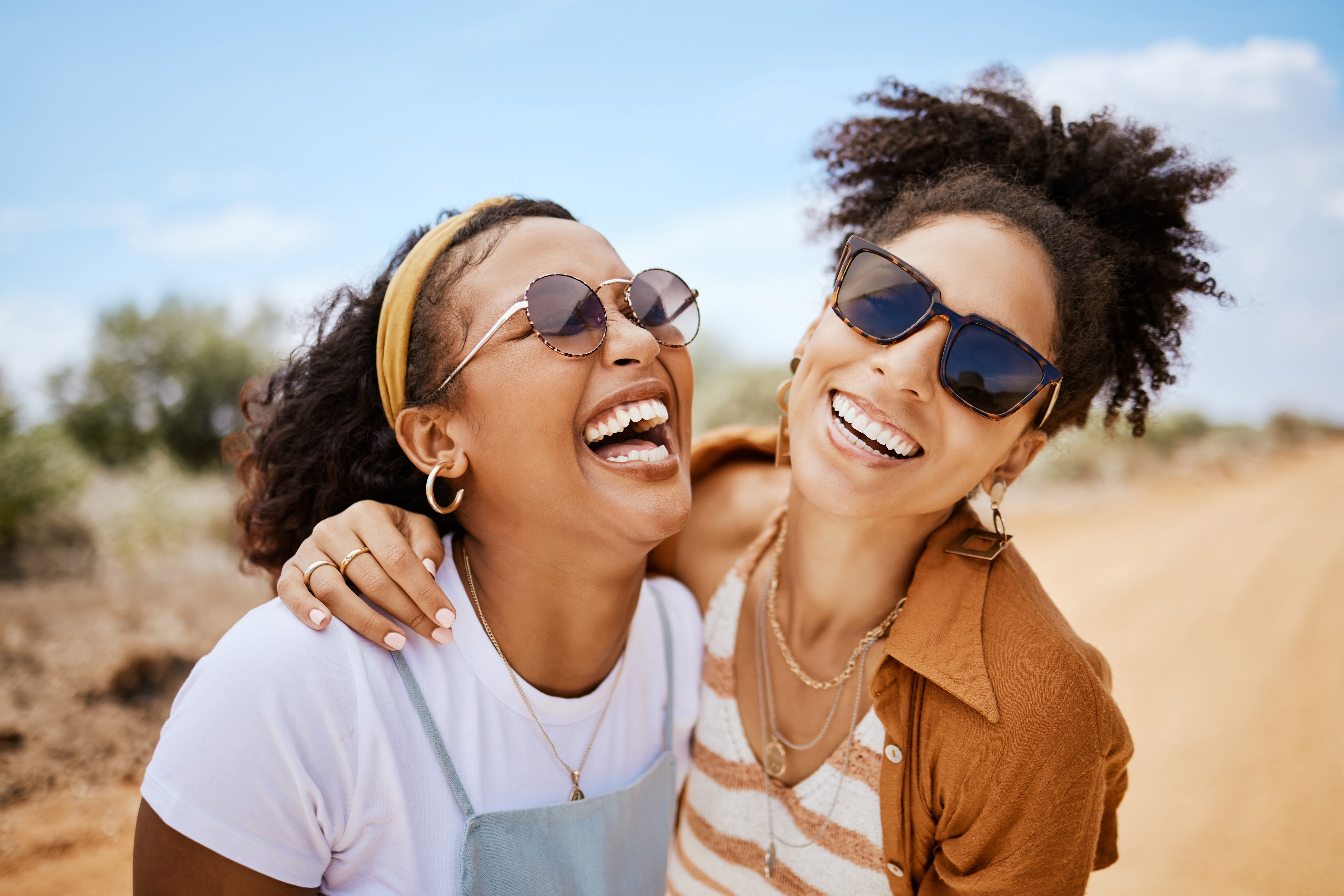Two women with sunglasses laughing together outdoors