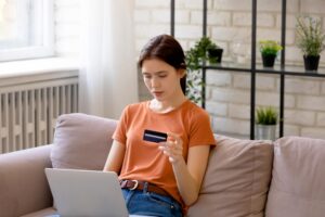 Young brunette woman looking at credit card with laptop in her lap