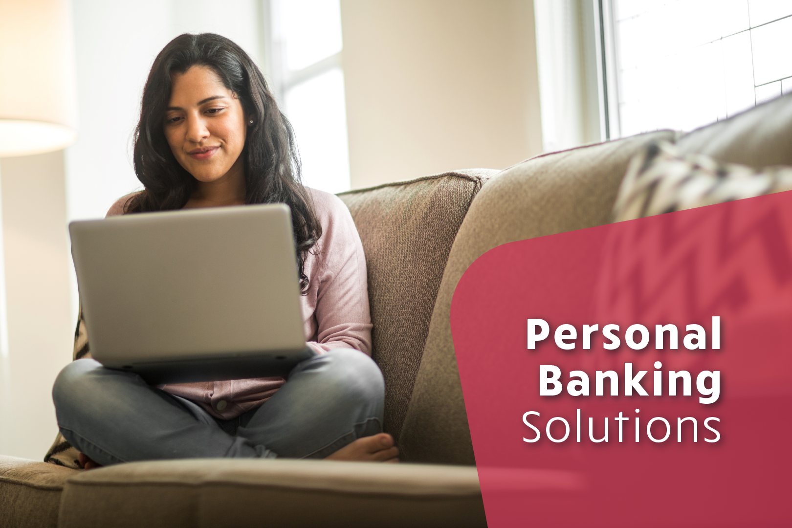 Photo of middle-aged woman with long brunette hair sitting with legs crossed on a couch with a laptop. Personal Banking Solutions