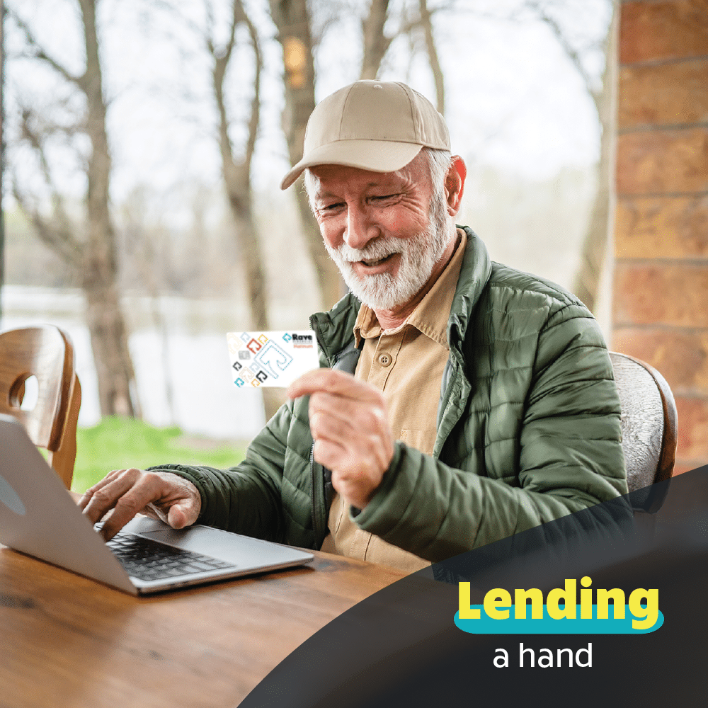 White male in his 60s wearing a baseball cap and sitting on his outdoor patio with his laptop open, looking at his Rave Visa Platinum credit card