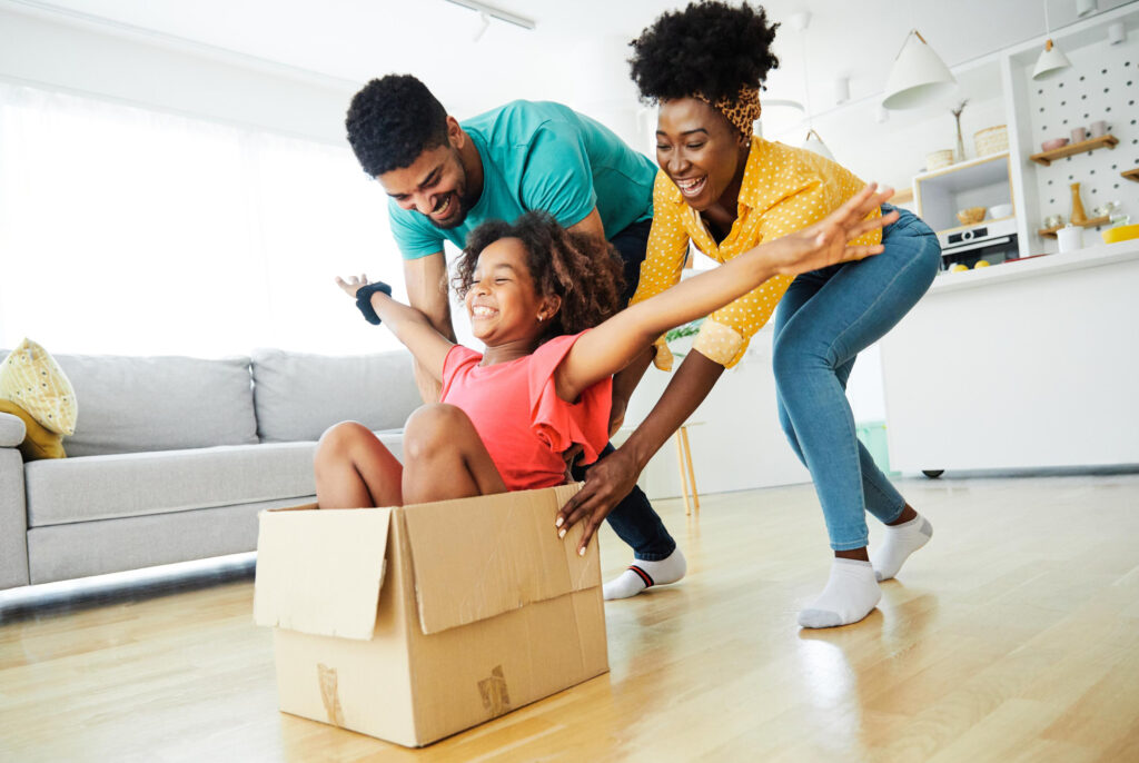 Mother and father pushing their young daughter in a moving box.