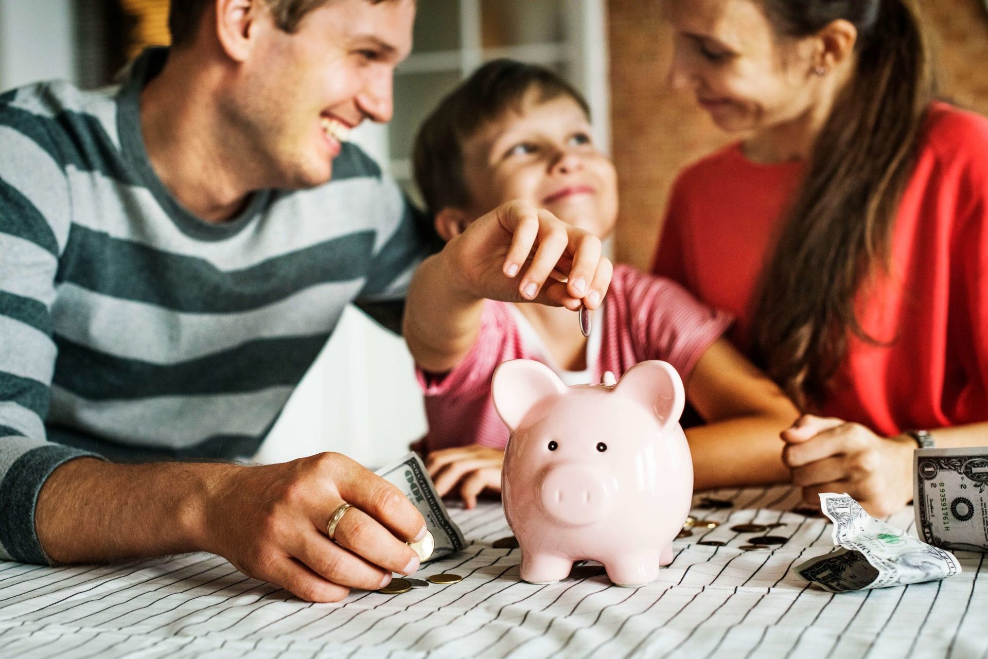 couple helping their kid put money into a piggy bank