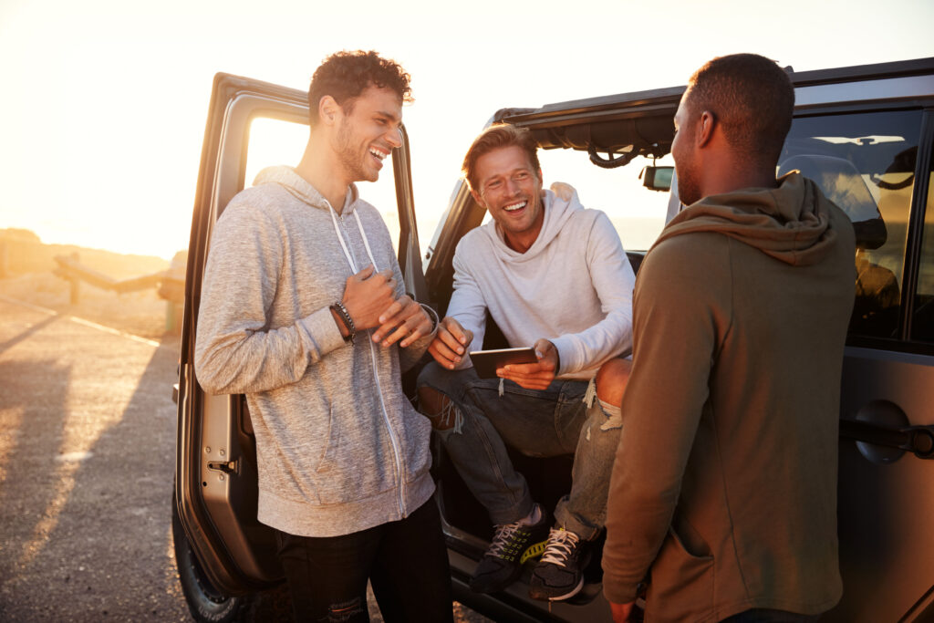 three young men talking next to a vehicle